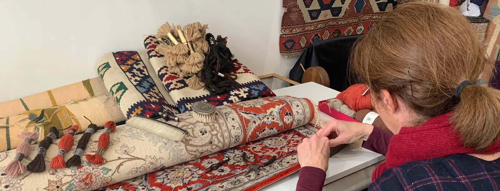 Reprise d'un tapis noué main à l'aiguille, laine teinte et outils posés sur la pièce